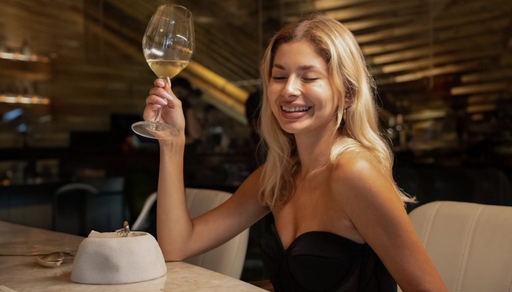 A woman sitting and  holding up a glass of wine at Table369.